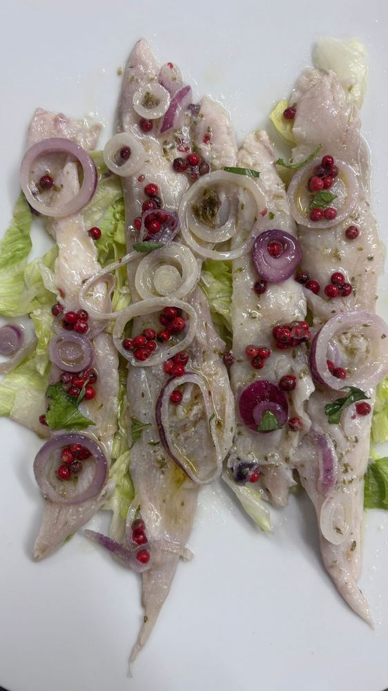 Alici marinate disposte a raggiera su insalata, con cipolla rossa e pepe rosa